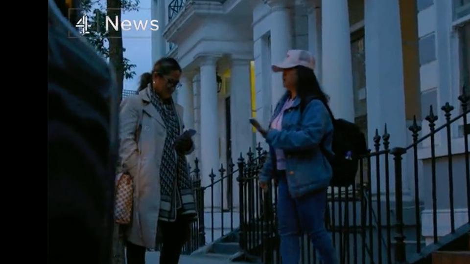 Video still shows two women waiting outside a large white house.