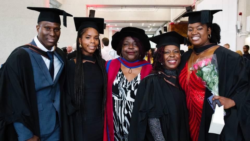 A group of four Black students pose with an academic at a graduation ceremony