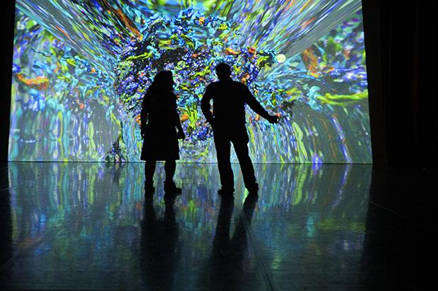 Two exhibition goers stand in front of a large blue digital art installation